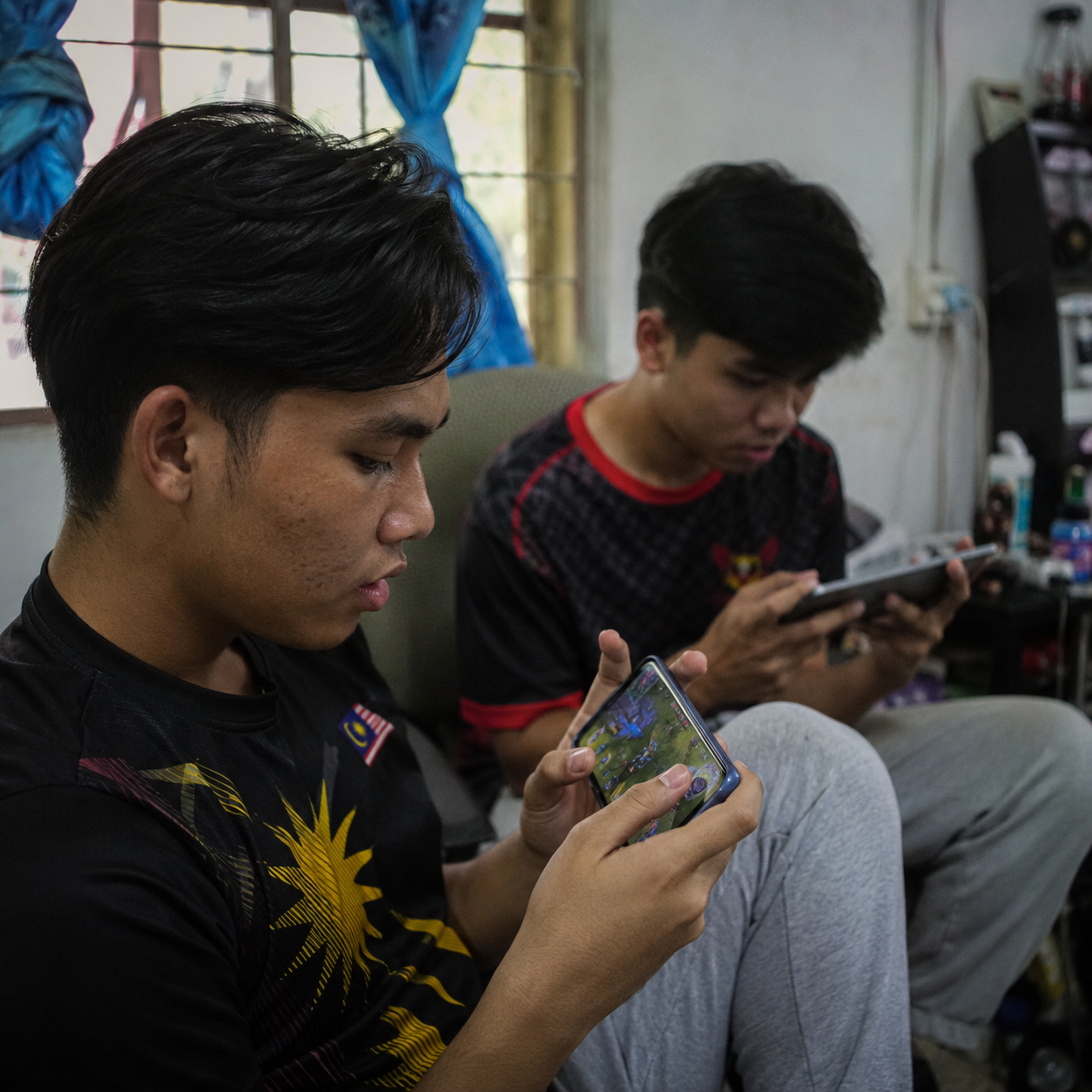 Young Malaysian playing mobile games at home during lockdown, natural window light, casual setting