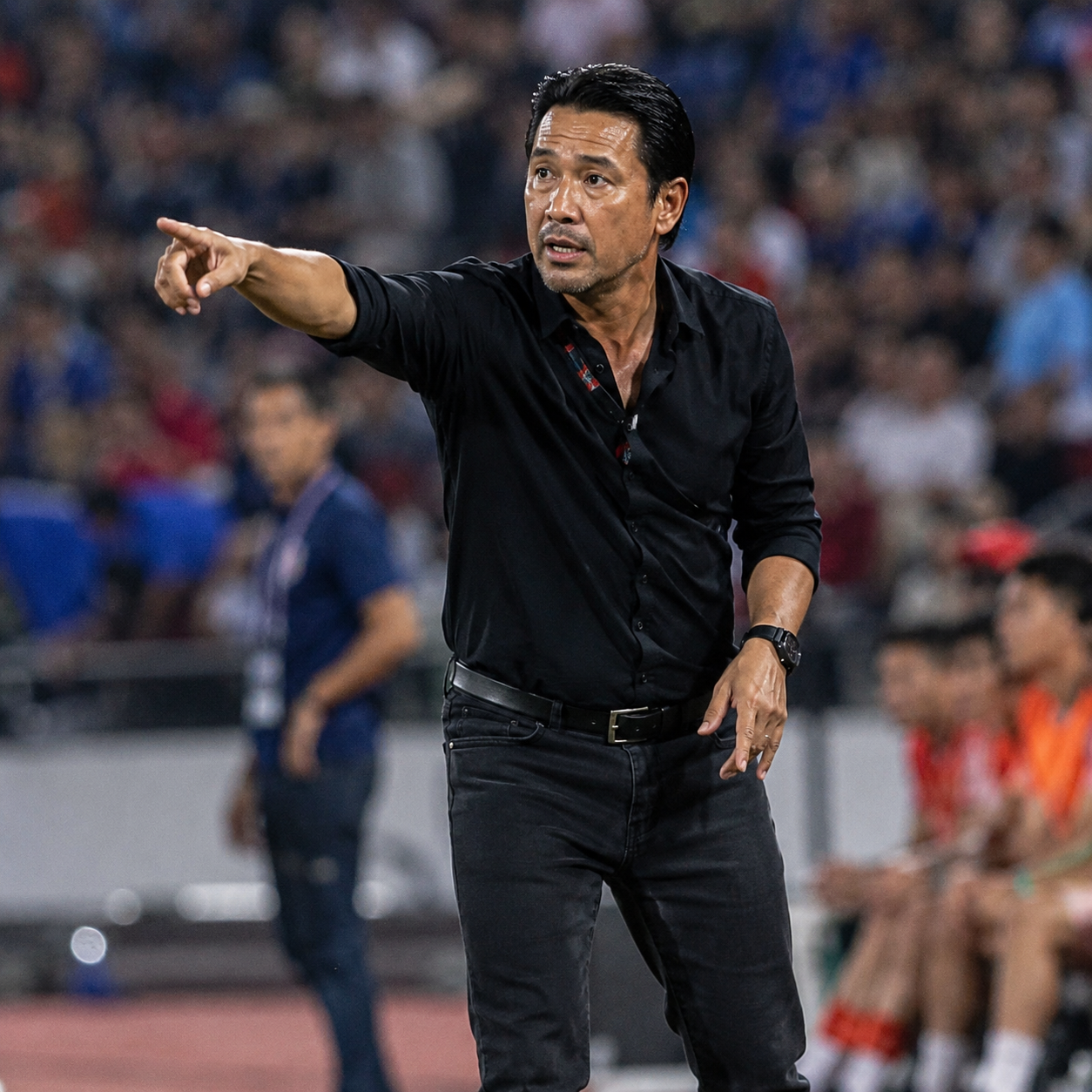 Football coach on touchline giving tactical instructions to players during match, stadium atmosphere, editorial sports photography