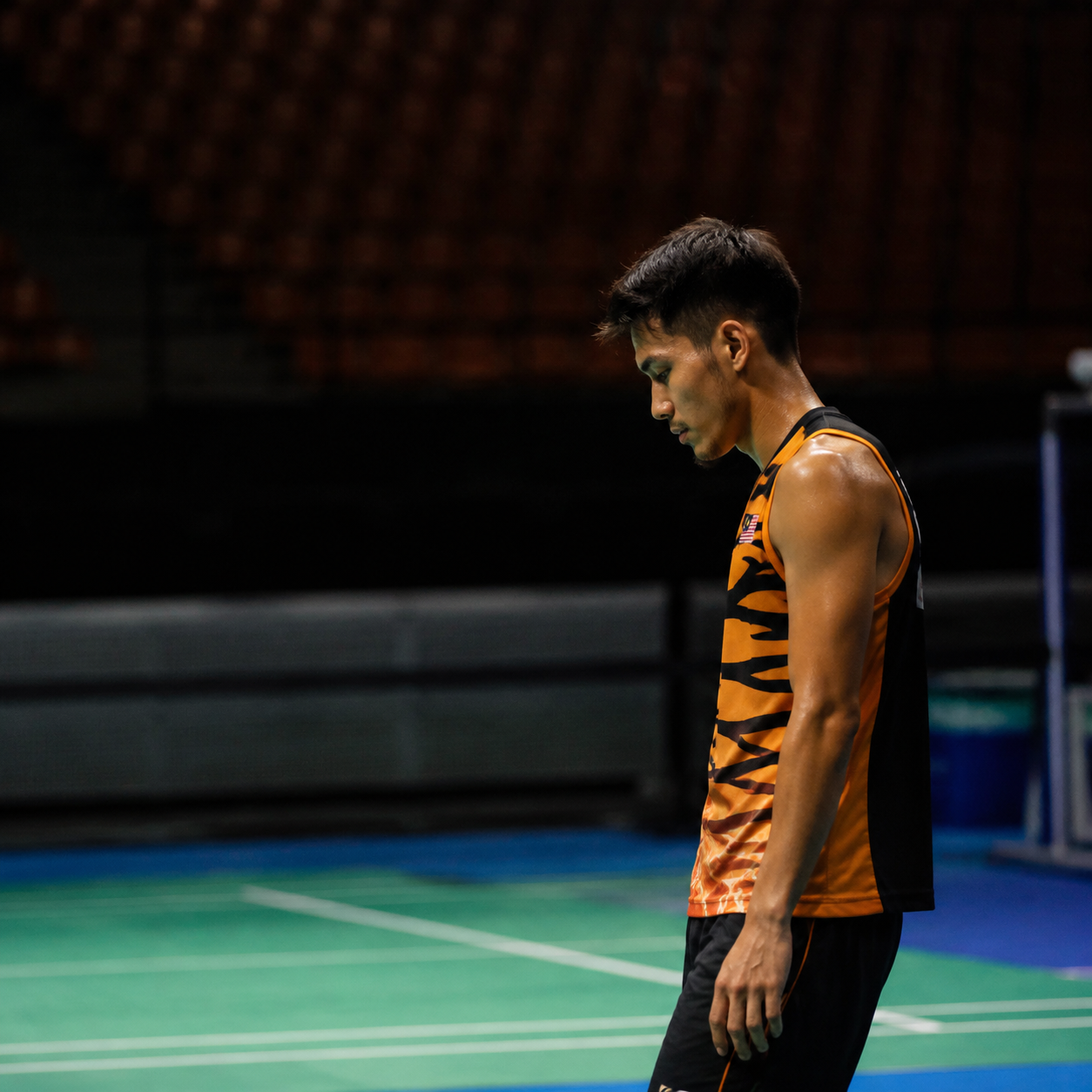 Athlete sitting alone on sports court, contemplative, indoor arena, natural window light, quiet emotional moment, editorial
