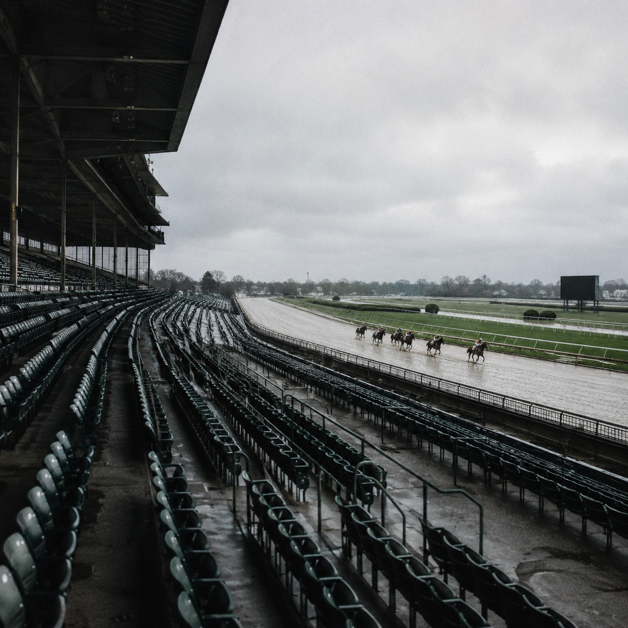 Empty grandstands at horse racing venue, horses racing on track, no spectators, atmospheric overcast sky