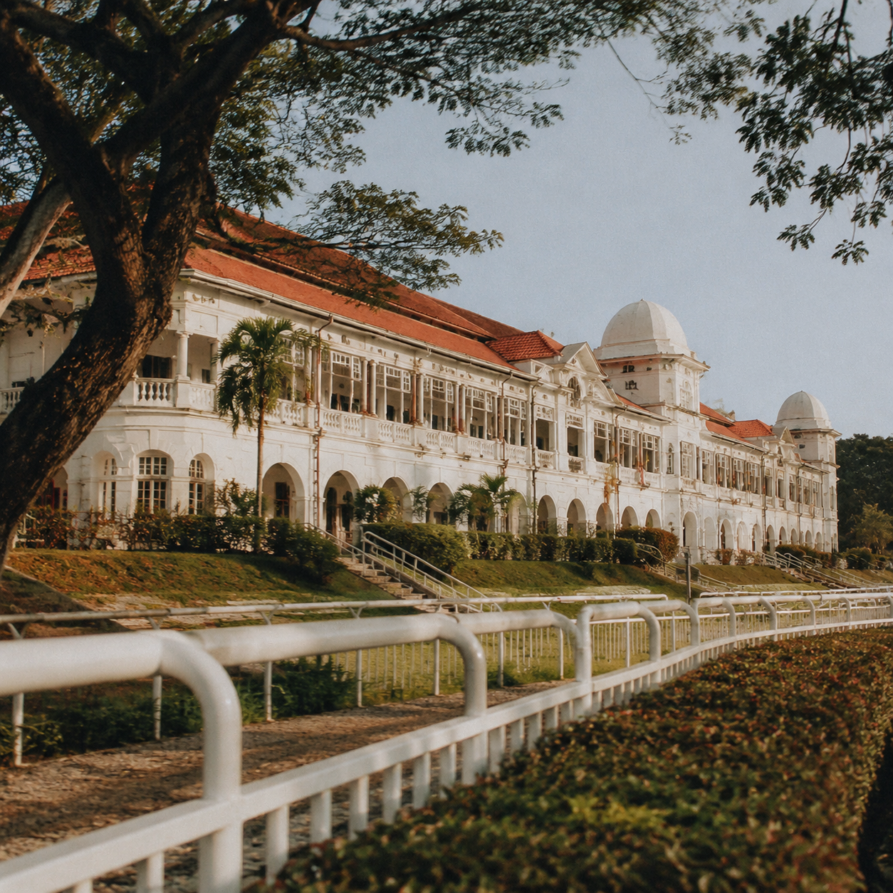 Historic horse racing club exterior, colonial-era architecture, tropical greenery, warm afternoon light, Malaysia