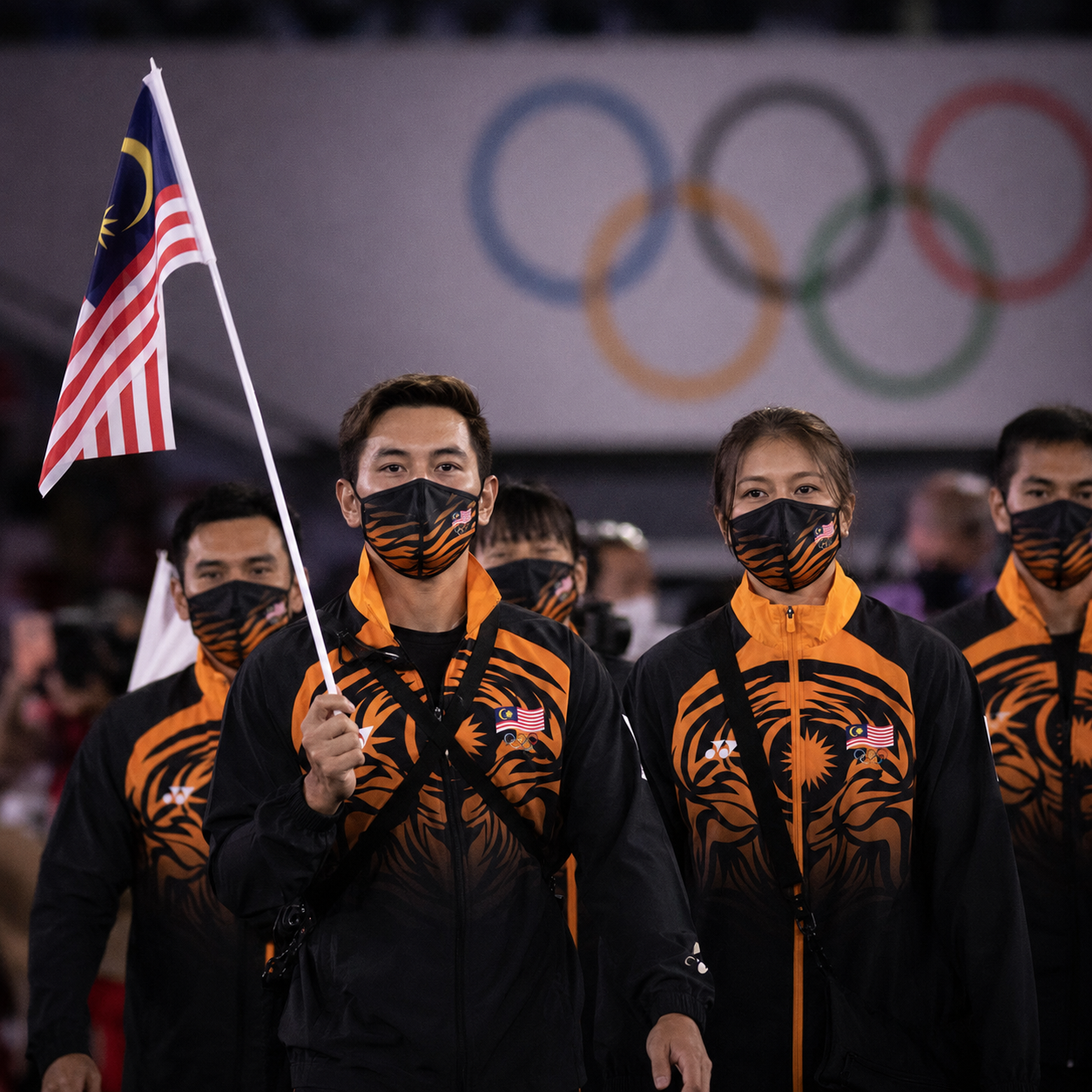Malaysian Olympic team athletes in national uniform at Tokyo Olympics, indoor venue, Olympic rings visible, realistic film grain