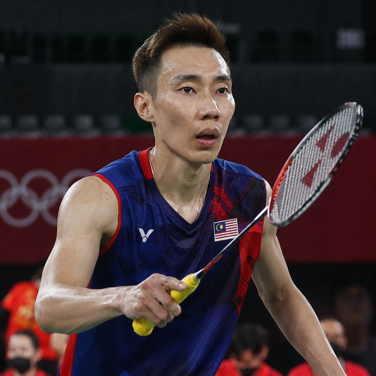 Badminton player at indoor Olympic competition, focused expression, indoor arena lighting, realistic film grain editorial